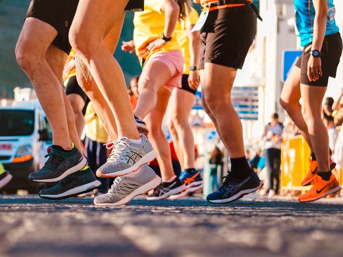 Runners' legs and athletic shoes mid-stride at a race start — biomechanical foot assessment, gait analysis, and custom orthotics context
